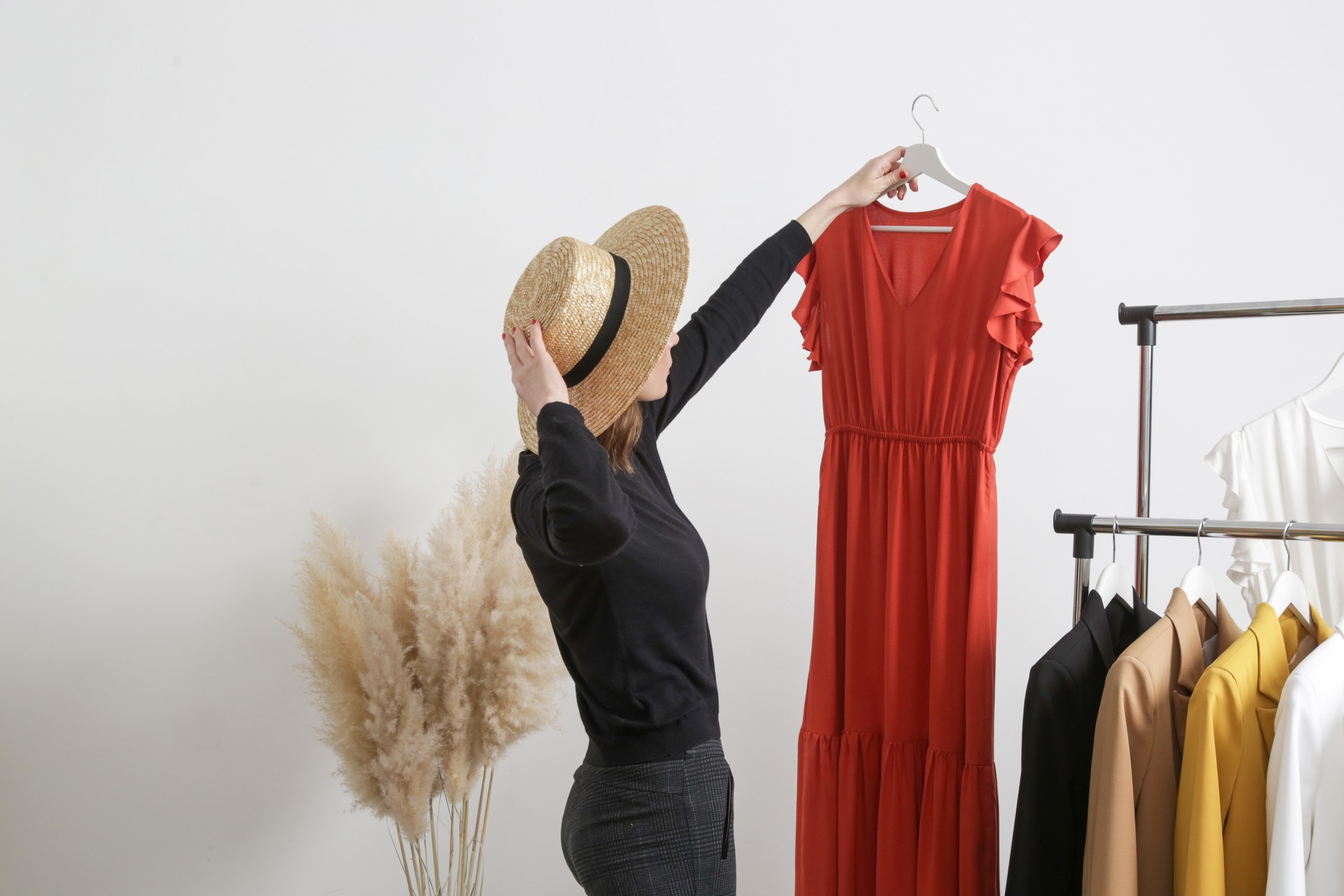 Beautiful young woman near rack with clothes holding long terracotta dress.